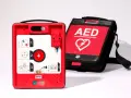 Czerwony defibrylator AED i jego czarna torba transportowa na białym tle.