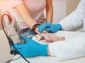Badanie EMG, czyli elektromiografia, to badanie oceniające funkcję nerwów i mięśni. Lekarz z niebieskimi rękawiczkami podłącza elektrody do ręki pacjentki.