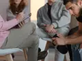 Grupa ludzi na sesji terapeutycznej, jedna osoba notuje.