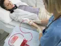Kobieta leży w łóżku szpitalnym, podłączona do kroplówki z krwią. Pielęgniarka monitoruje zabieg.