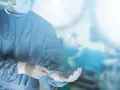 Chirurg w niebieskim fartuchu i masce zakłada rękawiczki w sali operacyjnej.