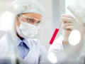 Naukowczyni w okularach i masce bada probówkę z czerwonym płynem. Wyniki wskazują na pct podwyższone.