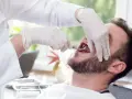 Dentysta w rękawiczkach używa kleszczy do usuwania zęba pacjentowi.