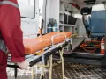 Nosze ratunkowe przed otwartą karetką, ratownik w czerwonej kurtce.