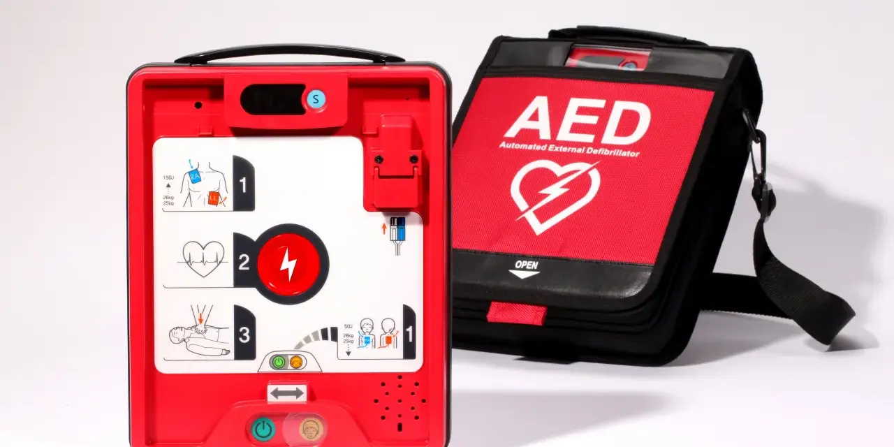 Czerwony defibrylator AED i jego czarna torba transportowa na białym tle.