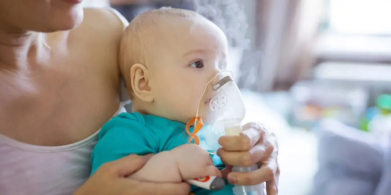Dziecko z maską inhalatora na twarzy, trzymane przez matkę.