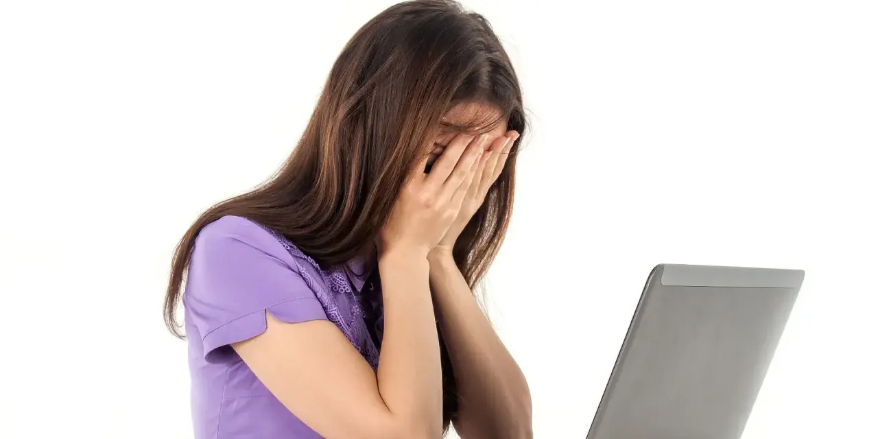 Kobieta zapatrzona w ekran laptopa, zakrywająca twarz dłońmi, emanująca apatią.