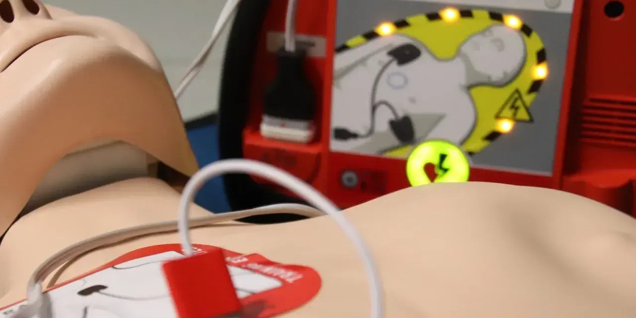 Defibrylator AED podłączony do manekina, gotowy do użycia.