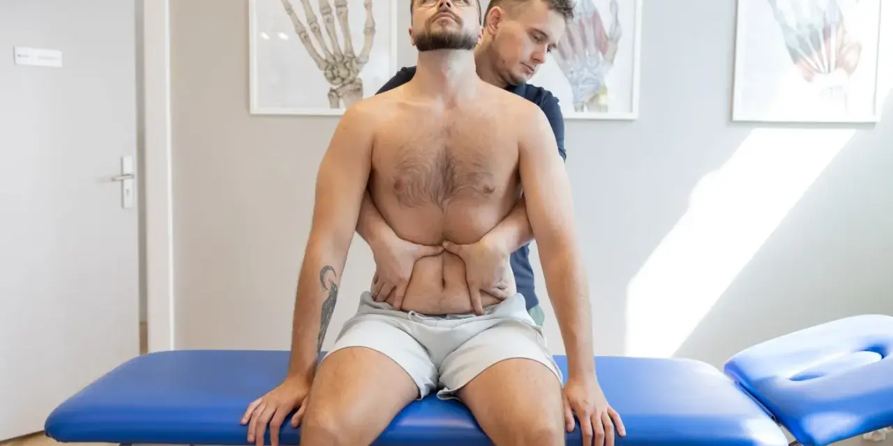 Terapeuta wykonuje terapię wisceralną, delikatnie uciskając brzuch pacjenta.