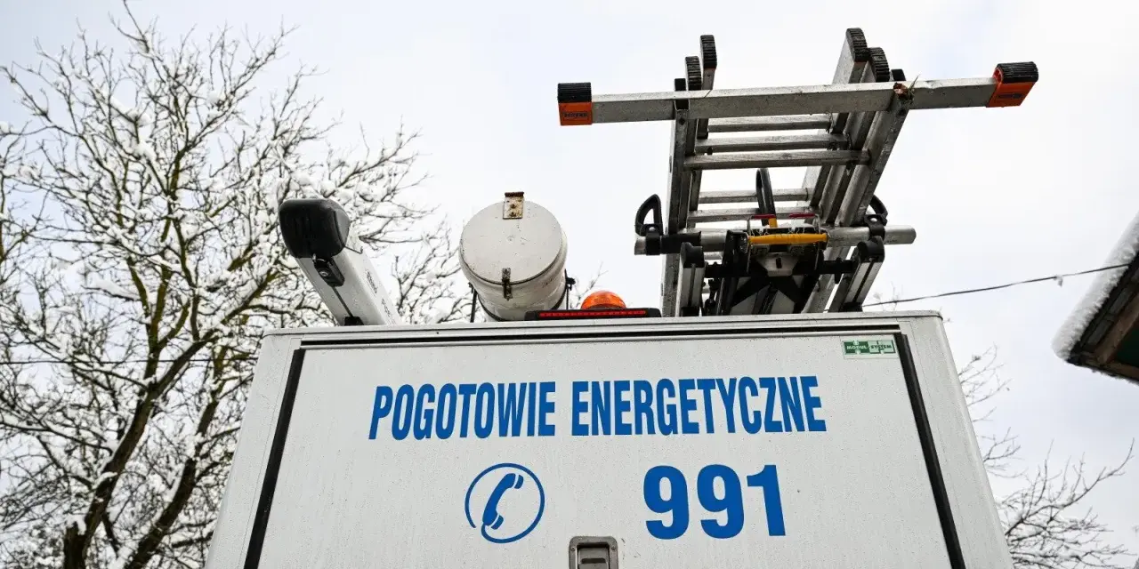 Tył białego samochodu pogotowia energetycznego z napisem "POGOTOWIE ENERGETYCZNE 991" i drabiną na dachu.