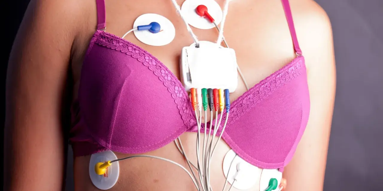 Kobieta w różowym biustonoszu z elektrodami EKG i rejestratorem Holtera na klatce piersiowej.