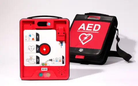 Czerwony defibrylator AED i jego czarna torba transportowa na białym tle.