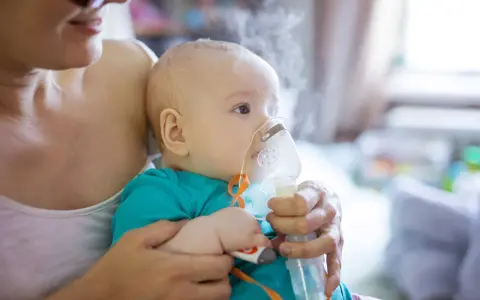 Dziecko z maską inhalatora na twarzy, trzymane przez matkę.