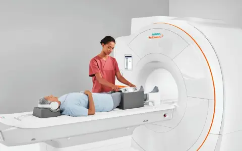 Pacjent leży na łóżku rezonansu magnetycznego, a technik przygotowuje jego nogi do badania. To właśnie mri co to za badanie, które pozwala zajrzeć do wnętrza ciała.