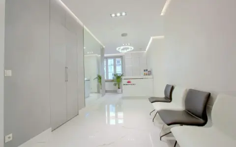 Nowoczesne wnętrze poczekalni kliniki estetycznej z białym recepcjonistą i wygodnymi fotelami.