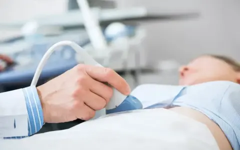 Lekarz wykonuje usg jamy brzusznej, przykładając głowicę do brzucha pacjentki. Przygotowanie do badania jest kluczowe.