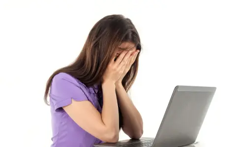 Kobieta zapatrzona w ekran laptopa, zakrywająca twarz dłońmi, emanująca apatią.