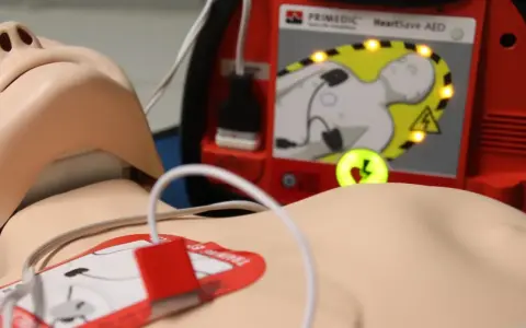 Defibrylator AED podłączony do manekina, gotowy do użycia.