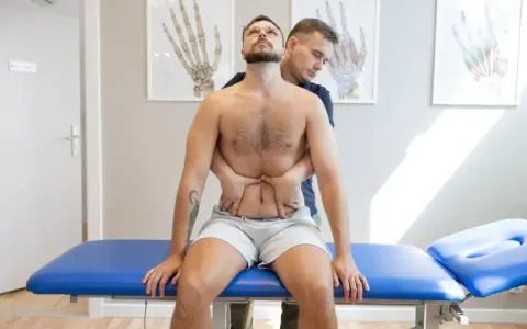 Terapeuta wykonuje terapię wisceralną, delikatnie uciskając brzuch pacjenta.
