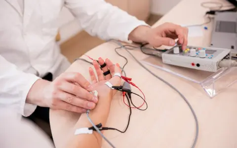 Lekarz wykonuje próbę tężyczkową, podłączając elektrody do dłoni pacjenta i regulując aparat.