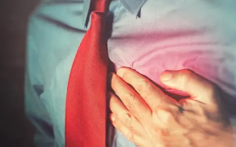 Mężczyzna w czerwonym krawacie trzyma się za serce, odczuwając ból. Może to być sygnał, by zadbać o swoje concor cor.