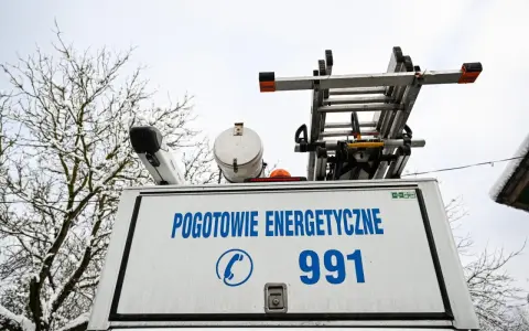 Tył białego samochodu pogotowia energetycznego z napisem "POGOTOWIE ENERGETYCZNE 991" i drabiną na dachu.