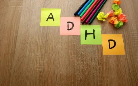 Kolorowe karteczki z literami "A", "D", "H", "D" układają się w napis ADHD. Obok leżą pisaki i pomięte papierki, jakby ktoś próbował znaleźć rozwiązanie, może z pomocą leku Elvanse.