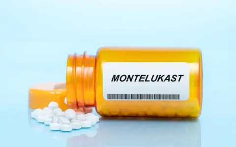 Pomarańczowa buteleczka z lekami, na etykiecie widnieje napis MONTELUKAST. Obok rozsypane białe tabletki.