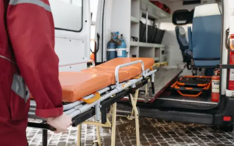 Nosze ratunkowe przed otwartą karetką, ratownik w czerwonej kurtce.