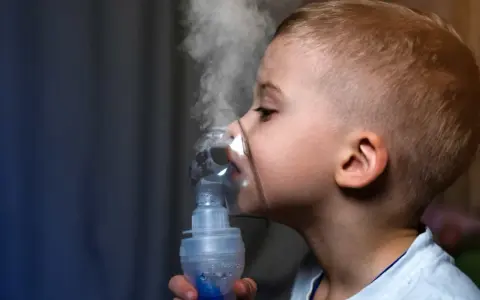 Chłopiec z maską inhalatora na twarzy, wdychający parę.