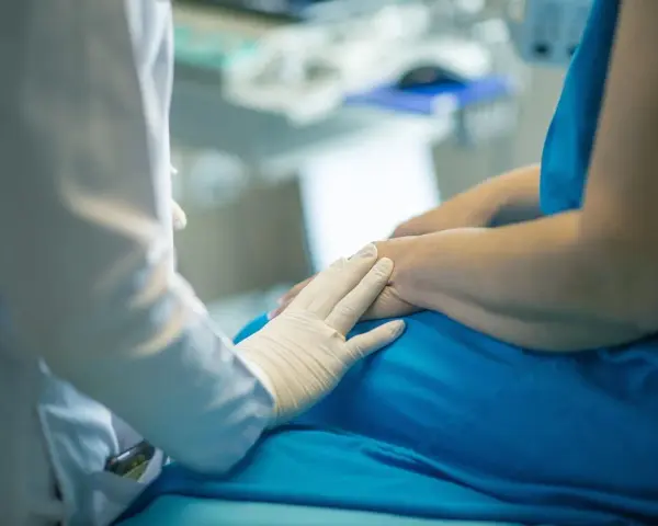 Lekarz w białej rękawiczce kładzie dłoń na ramieniu pacjenta w niebieskiej koszuli.