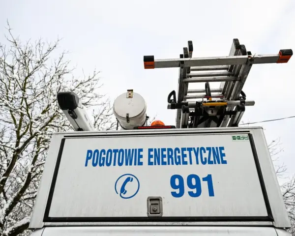 Tył białego samochodu pogotowia energetycznego z napisem "POGOTOWIE ENERGETYCZNE 991" i drabiną na dachu.