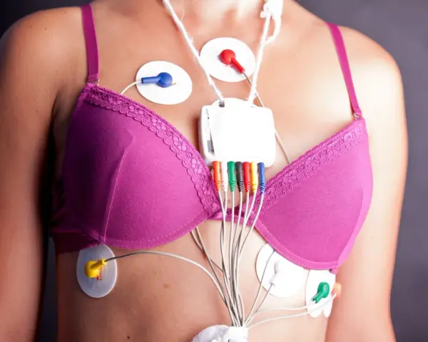Kobieta w różowym biustonoszu z elektrodami EKG i rejestratorem Holtera na klatce piersiowej.