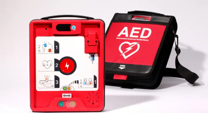 Czerwony defibrylator AED i jego czarna torba transportowa na białym tle.