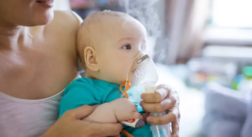 Dziecko z maską inhalatora na twarzy, trzymane przez matkę.