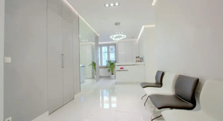 Nowoczesne wnętrze poczekalni kliniki estetycznej z białym recepcjonistą i wygodnymi fotelami.