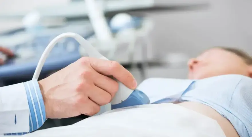 Lekarz wykonuje usg jamy brzusznej, przykładając głowicę do brzucha pacjentki. Przygotowanie do badania jest kluczowe.