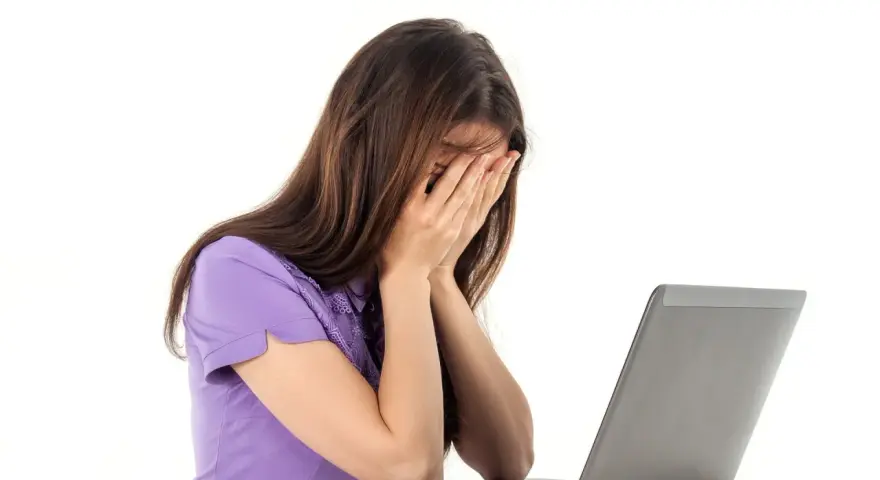 Kobieta zapatrzona w ekran laptopa, zakrywająca twarz dłońmi, emanująca apatią.