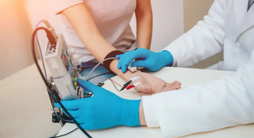 Badanie EMG, czyli elektromiografia, to badanie oceniające funkcję nerwów i mięśni. Lekarz z niebieskimi rękawiczkami podłącza elektrody do ręki pacjentki.