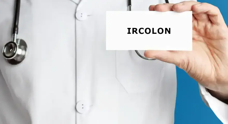 Lekarz w białym kitlu trzyma kartkę z napisem "IRCOLON". Stetoskop wisi na jego szyi.