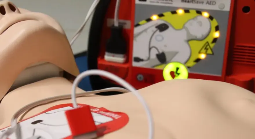 Defibrylator AED podłączony do manekina, gotowy do użycia.