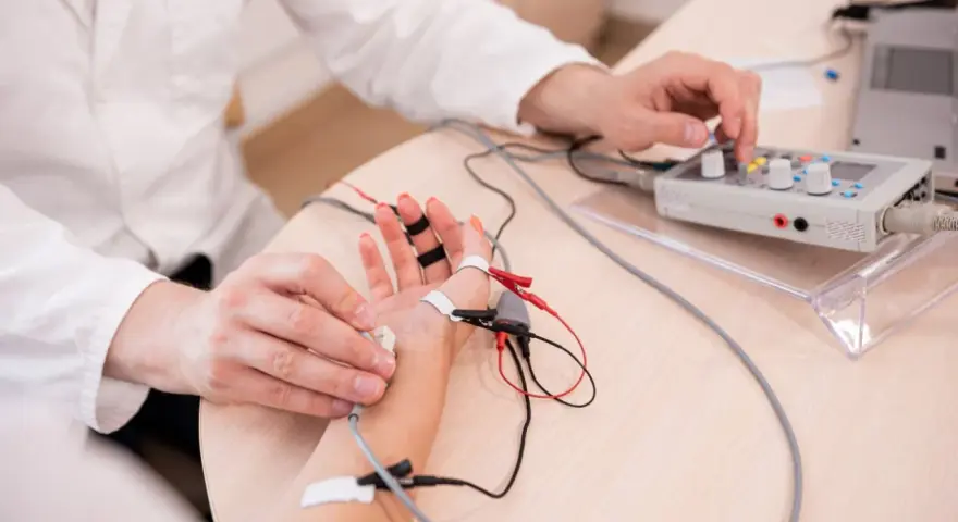 Lekarz wykonuje próbę tężyczkową, podłączając elektrody do dłoni pacjenta i regulując aparat.
