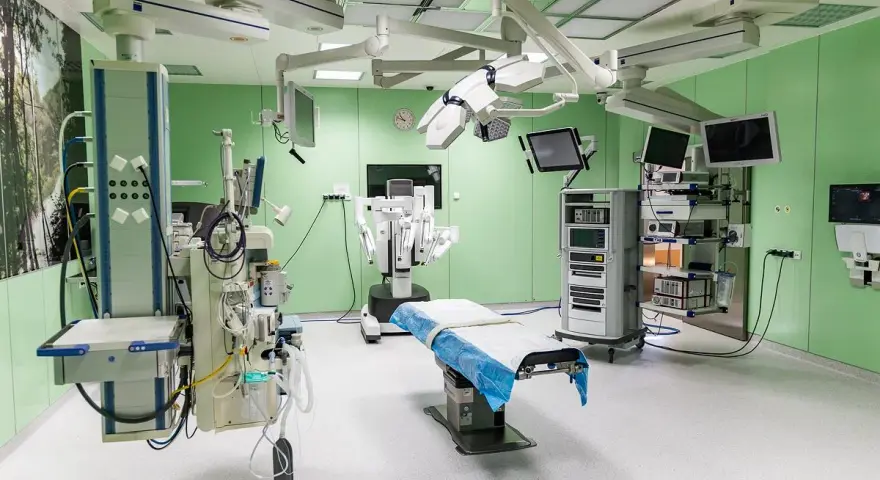Nowoczesna sala operacyjna z robotem da Vinci, stołem zabiegowym i aparaturą medyczną.
