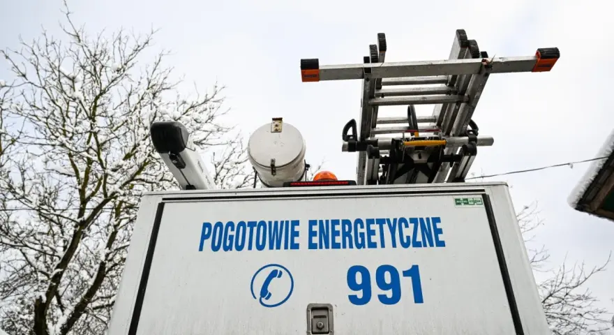 Tył białego samochodu pogotowia energetycznego z napisem "POGOTOWIE ENERGETYCZNE 991" i drabiną na dachu.