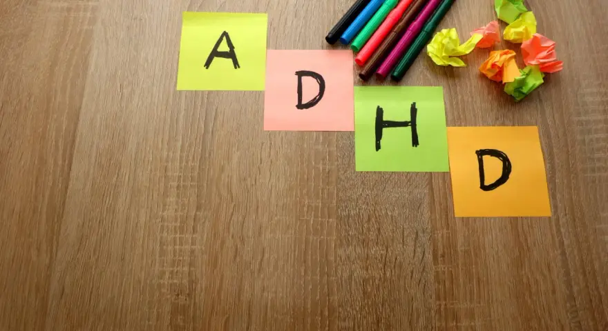 Kolorowe karteczki z literami "A", "D", "H", "D" układają się w napis ADHD. Obok leżą pisaki i pomięte papierki, jakby ktoś próbował znaleźć rozwiązanie, może z pomocą leku Elvanse.