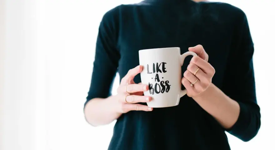 Kobieta trzyma kubek z napisem "Like a boss". Czy to pewność siebie, czy tylko maska na syndrom oszusta?