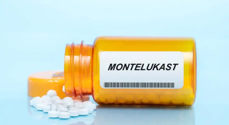 Pomarańczowa buteleczka z lekami, na etykiecie widnieje napis MONTELUKAST. Obok rozsypane białe tabletki.