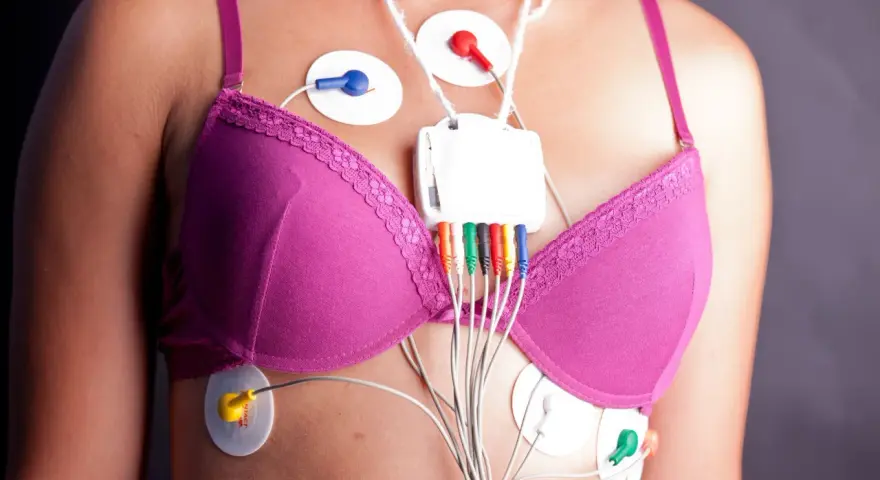 Kobieta w różowym biustonoszu z elektrodami EKG i rejestratorem Holtera na klatce piersiowej.
