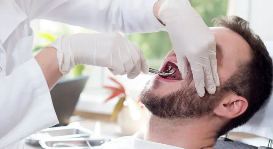 Dentysta w rękawiczkach używa kleszczy do usuwania zęba pacjentowi.