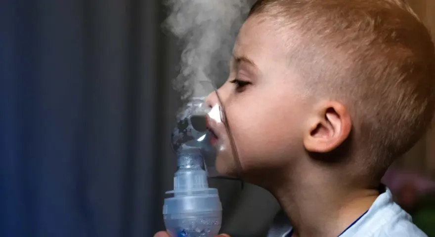 Chłopiec z maską inhalatora na twarzy, wdychający parę.